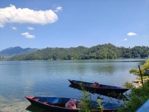 Two wooden boats moored on the calm shores of Begnas Lake with forested hills 