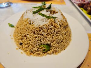 A plate of fragrant Kerala chicken rice garnished with fresh curry leaves and green chili. The warm colors and simple presentation highlight a popular South Indian dish enjoyed across Kerala. Captured in Kozhikode, Kerala. 