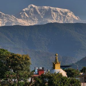 Golden Buddhist stupa with the watchful eyes of Buddha rising above Pokhara rooftops with the snow-capped Annapurna range behind
