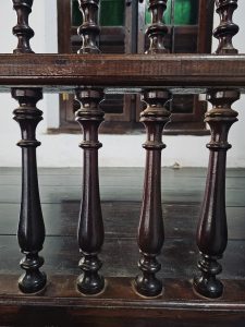 This detailed photograph focuses on the turned wooden balusters of a traditional railing. The repeating shapes and polished wood create a pleasing pattern that reflects the Arakkal Palace's heritage architecture. Captured at Arakkal Museum, Arakkalkettu, Kannur, Kerala.