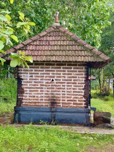 A small traditional Kerala-style shrine stands beneath a canopy of lush trees. The weathered tiled roof, brickwork, and surrounding greenery create a peaceful atmosphere that reflects the region's cultural and natural heritage. Captured at Thondayad, Kozhikode, Kerala. 