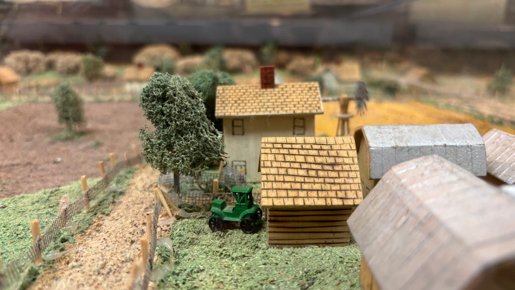 Closeup of a small scale model of a farm. There are two houses and a green tractor.