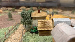 Closeup of a small scale model of a farm. There are two houses and a green tractor.
