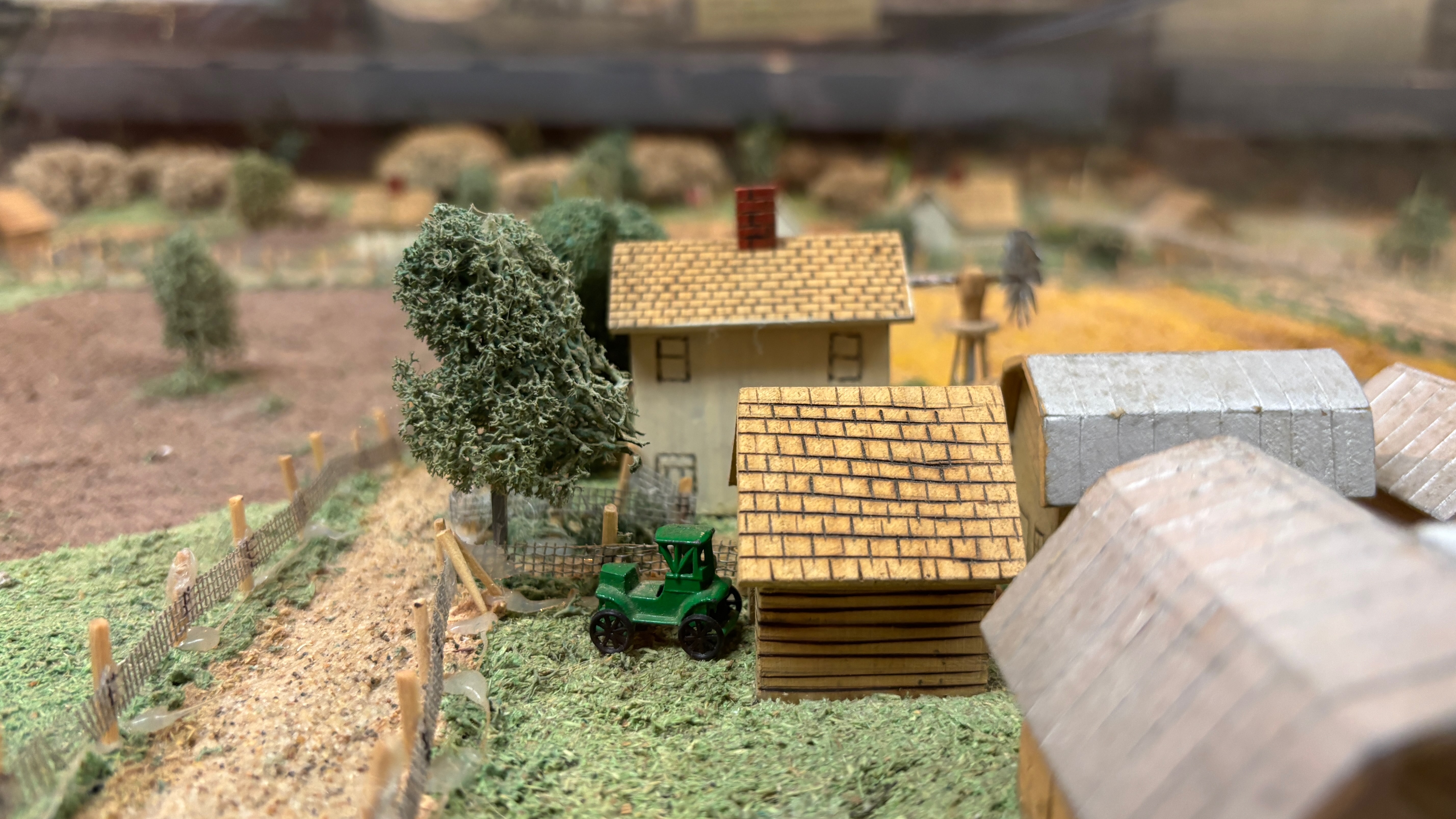 Closeup of a small scale model of a farm. There are two houses and a green tractor.