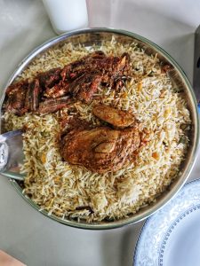 A metal tray filled with aromatic biryani rice, topped with spicy grilled beef and chicken.