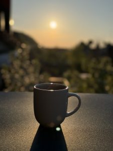 A white ceramic mug sits on a sleek, dark surface, casting a soft shadow as the sun sets in the background.