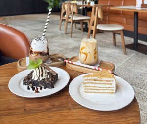A cafe table spread with a chocolate brownie with ice cream, a honey layer cake slice, a chocolate frappe with whipped cream, and an iced caramel latte at a modern cafe in Nepal. 