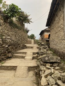 A narrow stone paved alley winding uphill between old stone walled houses in a traditional Nepali mountain village.