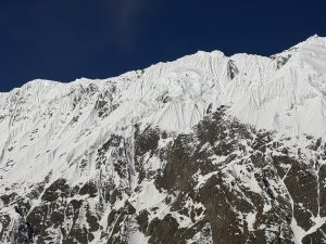 Dramatic close-up of a massive snow-streaked Himalayan wall against a deep blue sky  