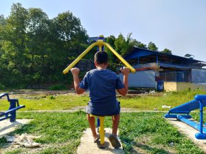A boy using a lat pulldown machine at an outdoor public fitness park in Nepal. 