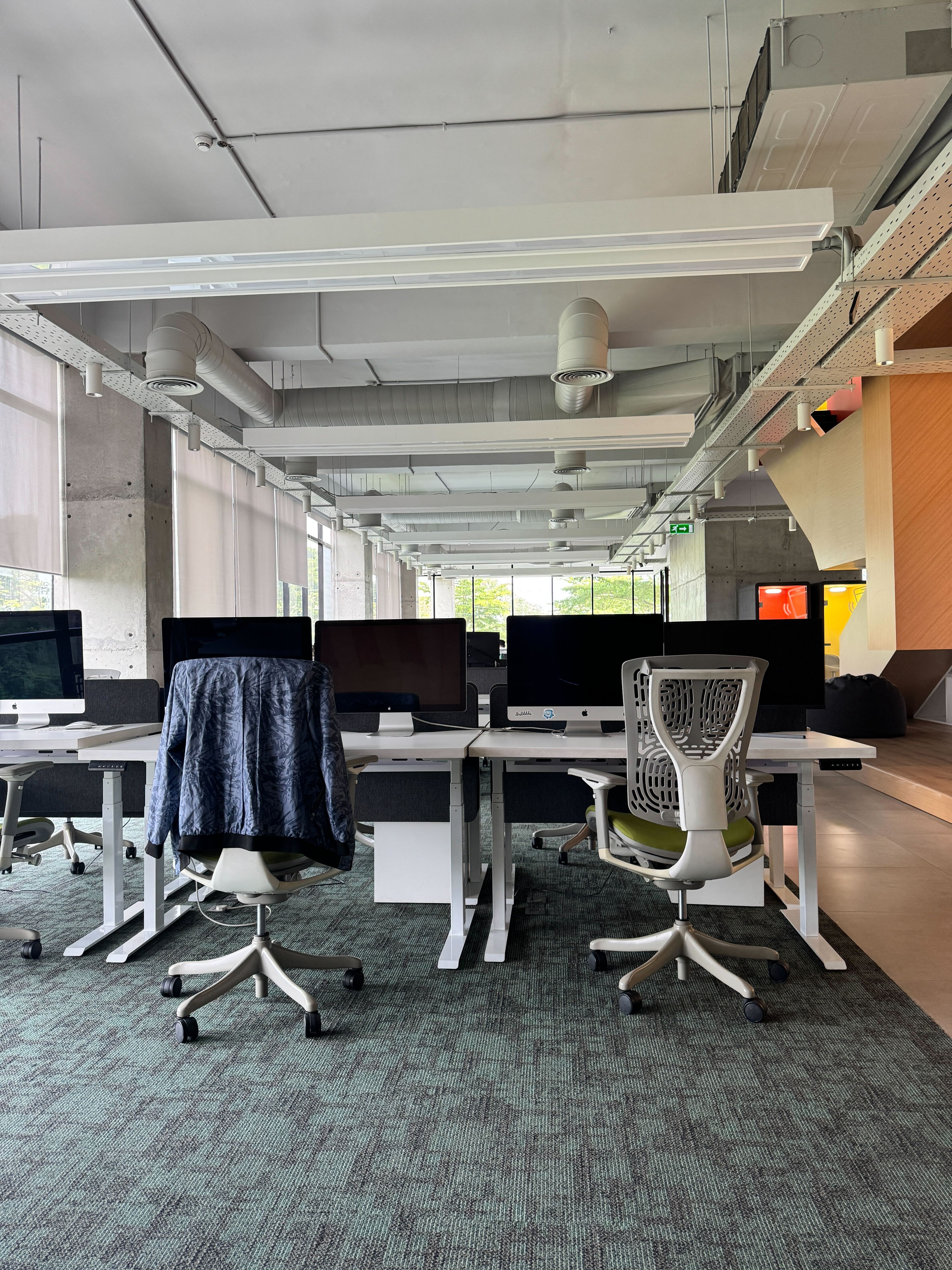 Modern office space featuring rows of desks with computers, ergonomic chairs, and large windows.