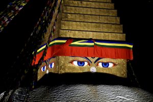 The Boudhanath Stupa in Kathmandu glows under the night sky, its golden spire and painted Buddha eyes illuminated with vibrant prayer flags stretching outward. 
