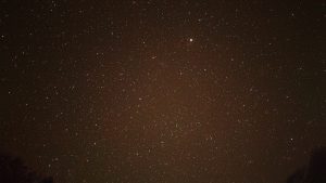 Countless stars scattered across a vast warm-toned night sky with a single bright planet glowing at the center 