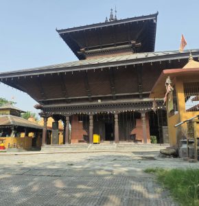 

A traditional Nepalese temple Bolbom Dham  with intricate wooden carvings and a tiered roof stands under a clear blue sky