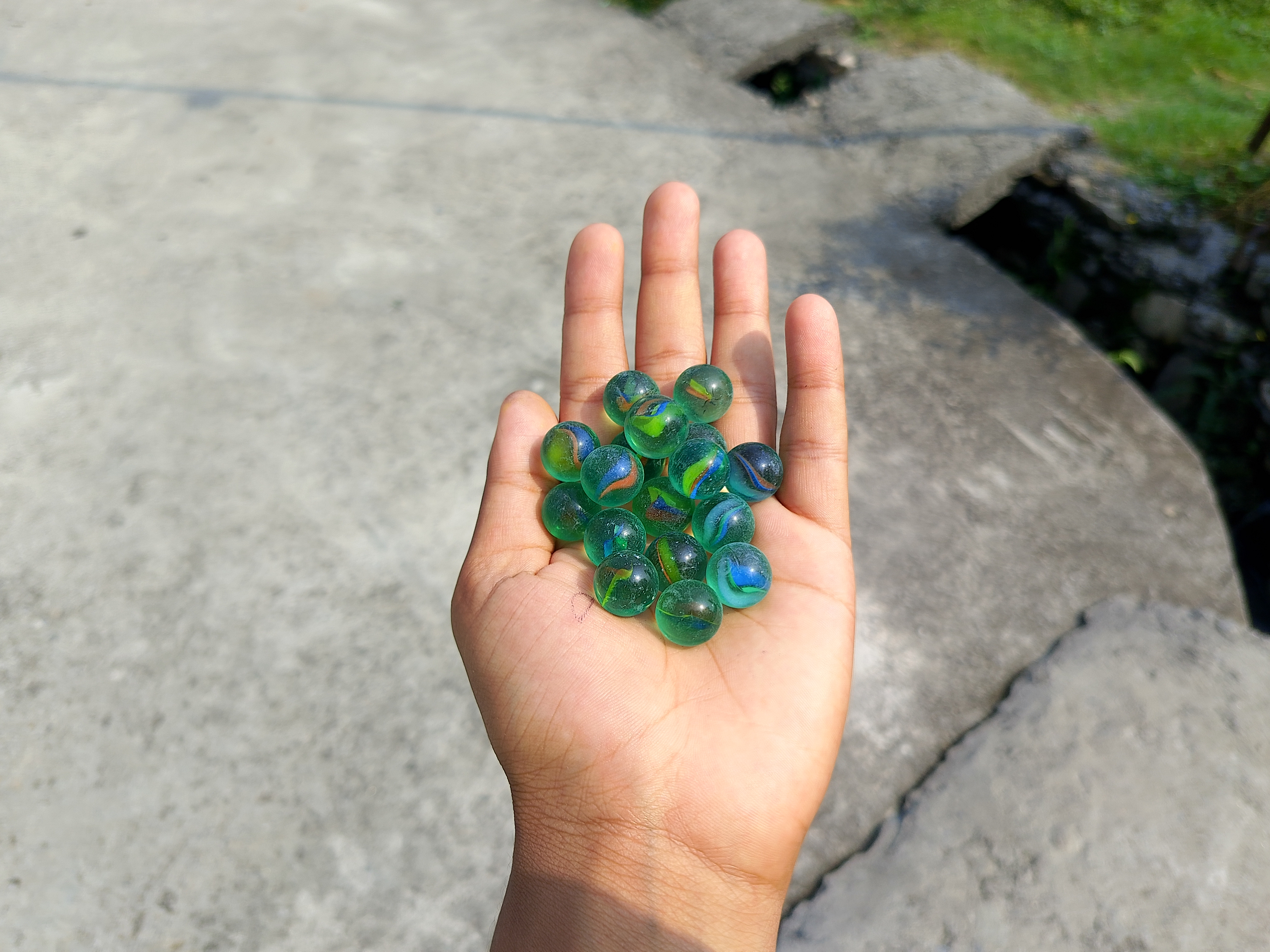 Hand holding green glass marbles glinting in sunlight.