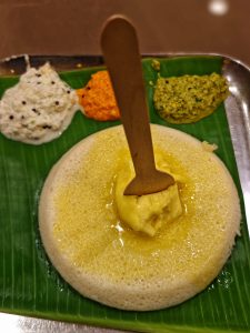 Butter idily served on a green leaf with three different types of chutney aside 
