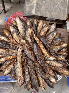 Smoked whole fish arranged in a circular fan pattern on a wooden surface at a market stall. 