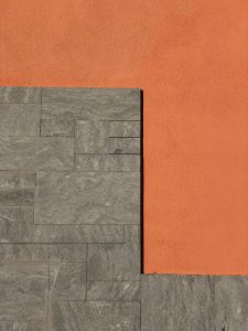 A wall with a L shape pattern, half on orange concrete and other half on gray rock bricks