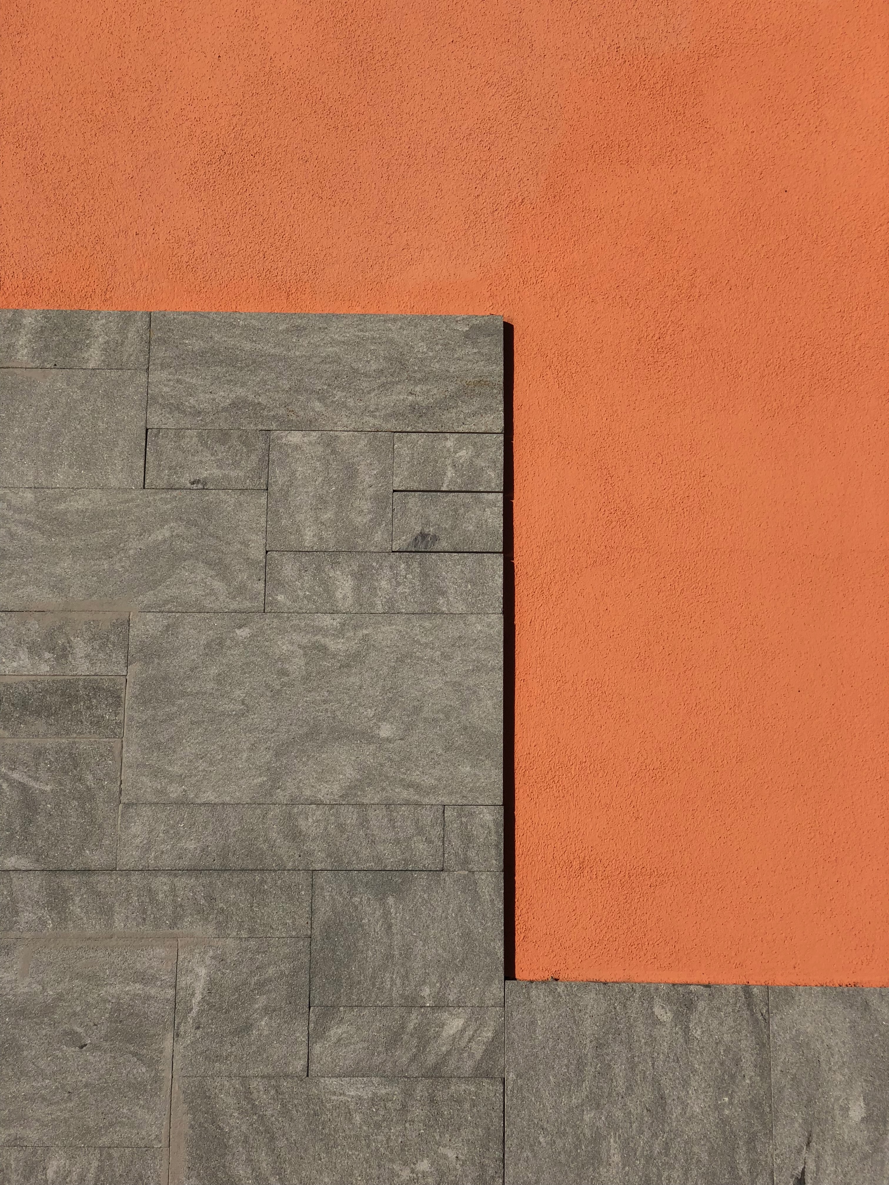 A wall with a L shape pattern, half on orange concrete and other half on gray rock bricks