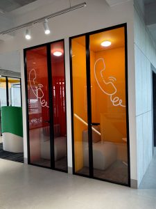 Bright, open office space featuring two glass-walled phone booths with vibrant orange and red interior walls and telephone graphics.