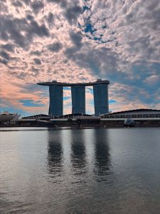 Marina Bay Sands reflected in calm waterfront waters beneath dramatic cloud formations in Singapore. 