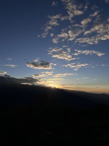 Sunrise over a mountain range with a clear blue sky. Scattered clouds catch early golden light,