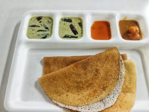 A crispy dosa served on a white tray with three chutneys