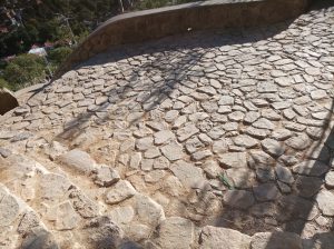 Stone-paved pathway with irregular rocks and shadows cast across the surface.