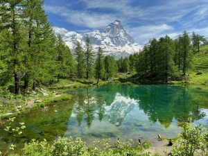 Cervino mountain peak with snow reflected on an small lake surrounded by trees