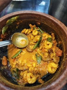 Rich and aromatic prawn curry with curry leaves simmering in a traditional clay pot with a ladle 