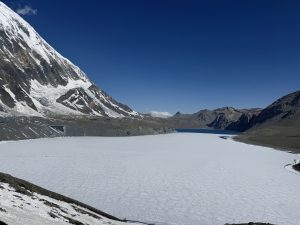 Frozen Tilicho Lake at 4,919m — one of the world's highest lakes — flanked by a towering snow-covered Himalayan peak 