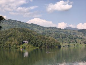 Begnas Lake sign on a forested hillside reflected in calm waters with terraced farmland beyond 