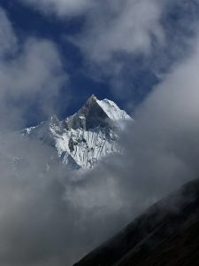 
Snow-capped mountain peak piercing through swirling clouds against a deep blue sky, conveying a sense of majesty and mystery.