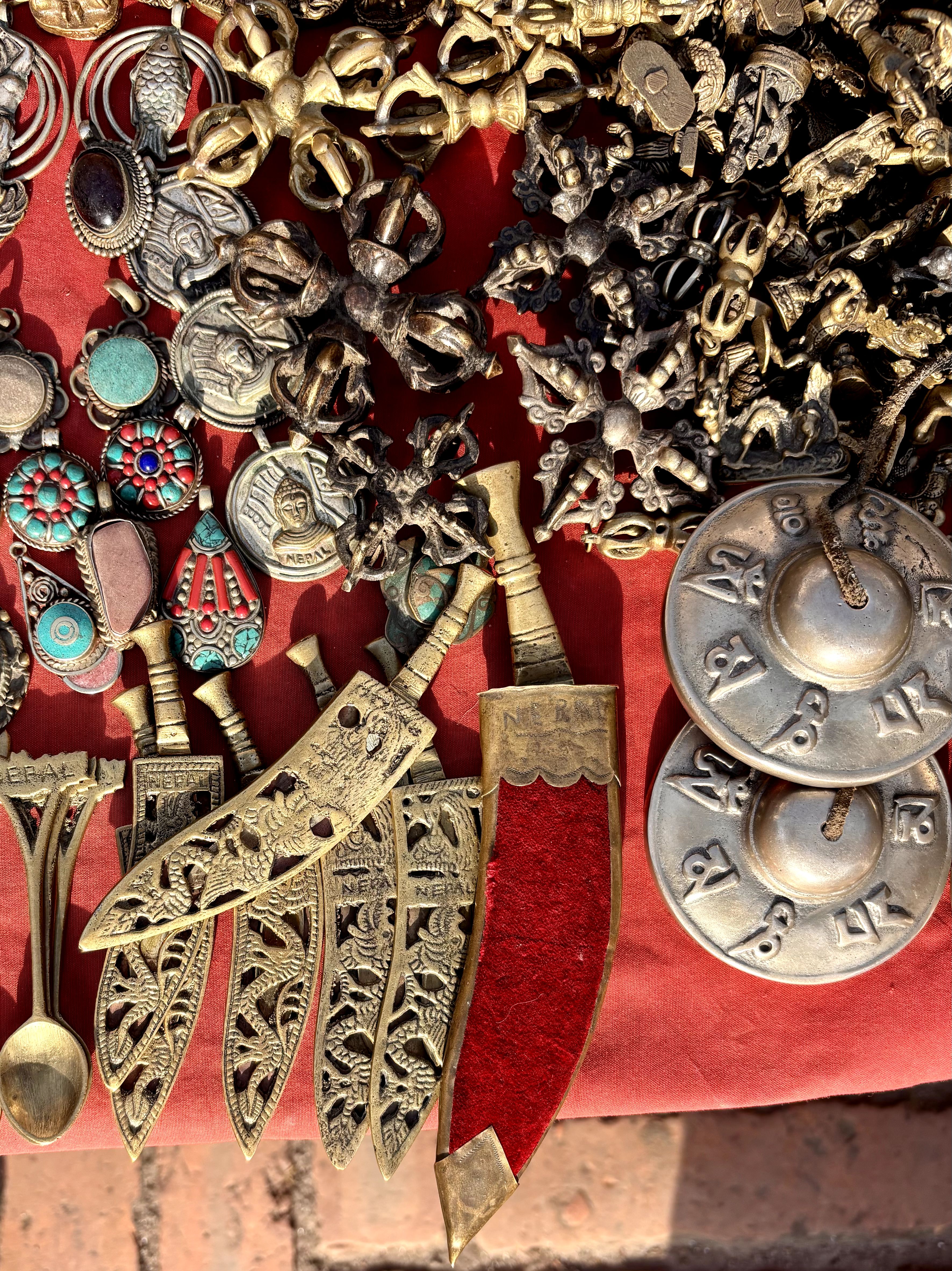 Traditional Nepali souvenirs including brass khukuri knives, tingsha cymbals, and turquoise jewelry on red cloth.