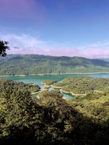 Emerald lake with forest-covered islands and misty hills under a blue sky. 