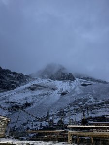 Snow covered mountain peaks shrouded in mist under a cloudy sky. Colorful prayer flags hang in the foreground