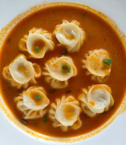 Soup momo (dumplings) in spicy orange broth, garnished with spring onions.