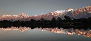 Annapurna range glowing pink at sunrise perfectly mirrored in a still alpine lake with silhouetted mountain huts 