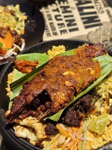 Grilled fish with spicy marinade on banana leaf, served on a bed of yellow rice, accompanied by mixed vegetables. 
