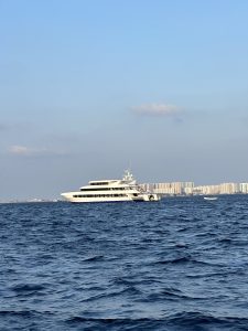 A white boat resting on a calm sea with the city landscape behind it.