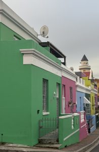 Colorful row of houses in green, pink, and blue shades with white trim in a narrow street under a cloudy sky