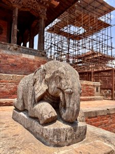 A weathered stone elephant sculpture at a Newari temple under reconstruction with scaffolding in Patan Durbar Square, Nepal.