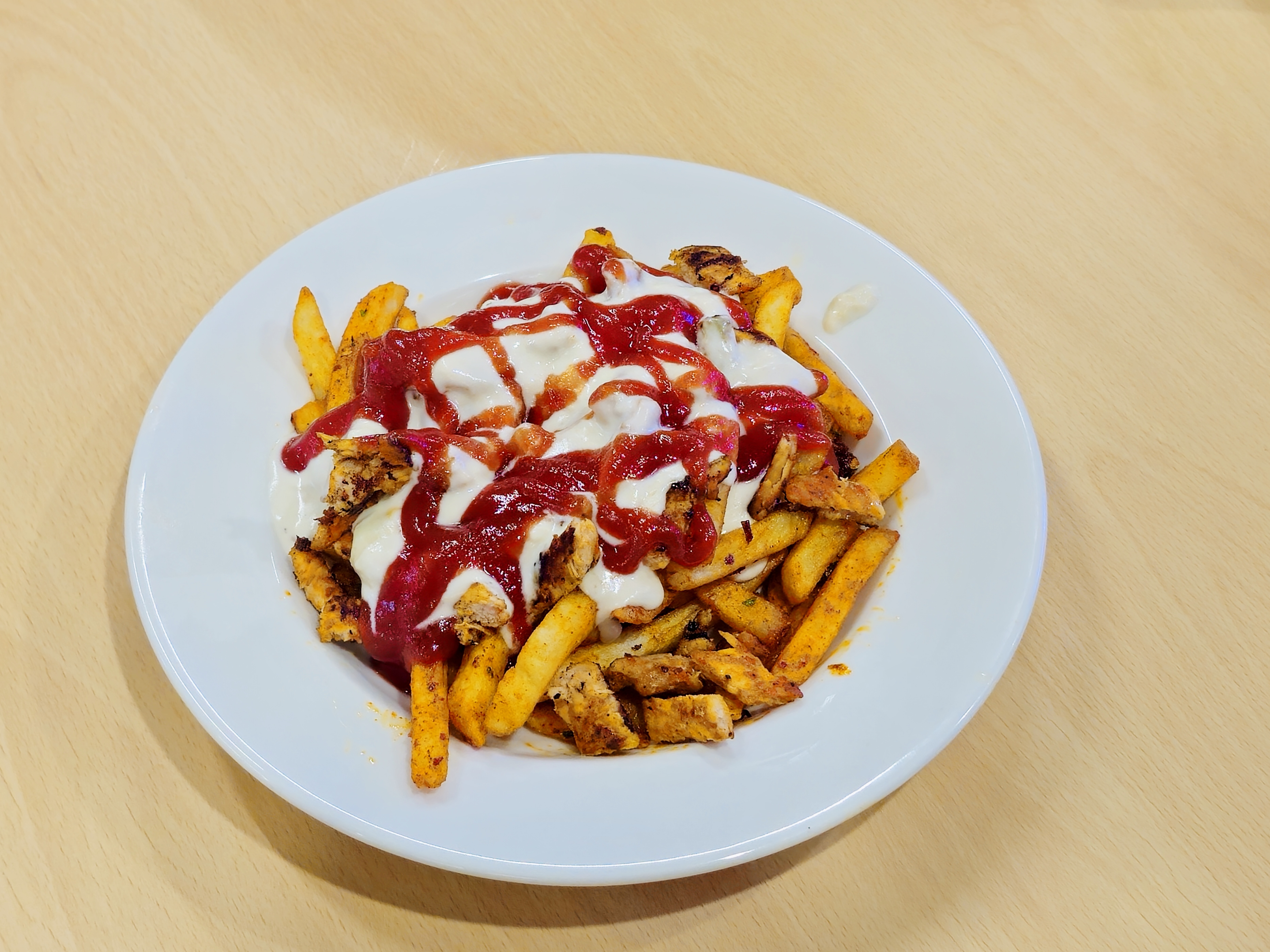 A plate of crispy seasoned fries topped with grilled chicken, creamy mayonnaise, and tangy tomato sauce makes for a delicious and colorful meal. Captured in Kannur, Kerala.