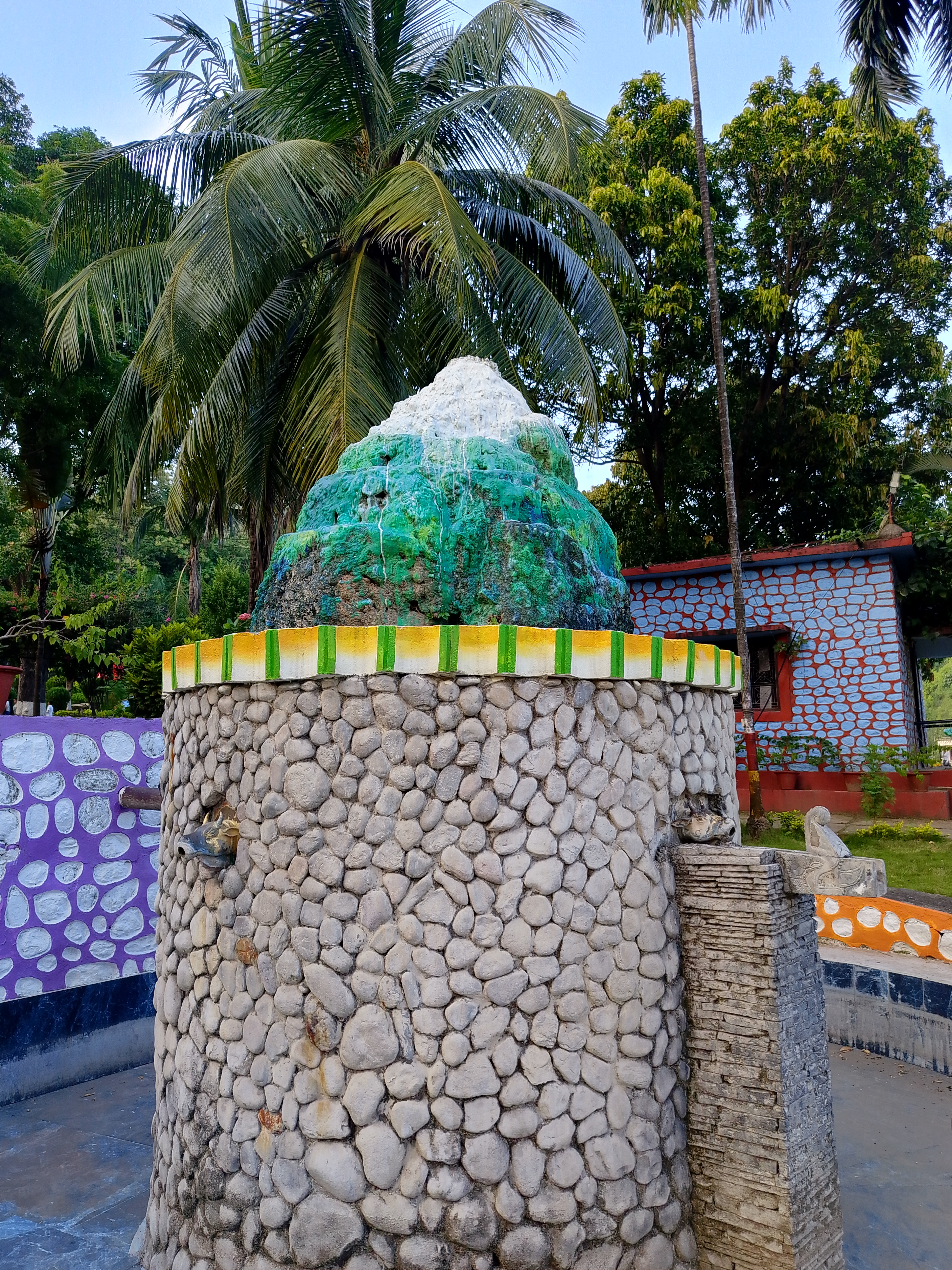 Decorative stone-cobbled fountain structure topped with a painted mountain replica in a park