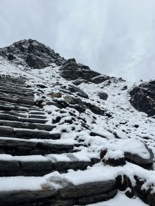 Snow-covered stone steps lead upward along a rugged mountainside, creating a serene and chilly atmosphere under a gray, overcast sky.