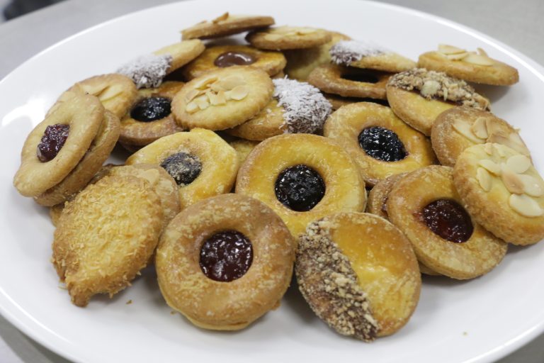 Plate of assorted round cookies with various toppings like jam, chocolate, coconut, nuts, and almond slices.