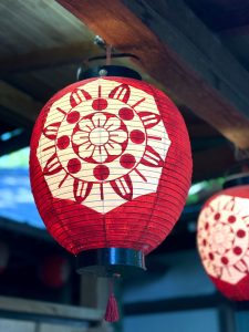 A beautifully crafted Japanese paper lantern glowing beneath a wooden roof, showcasing the elegance of traditional Japanese design.