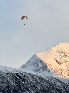 paragliding high above a snow-covered mountain range with golden sunlight