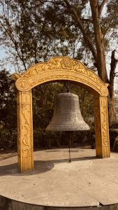 World Peace Bell in Lumbini. A large, ornate bronze bell hangs suspended by a chain beneath a decorative golden archway.
