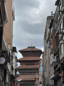 Tall pagoda-style temple with red brick and tiered roofs framed by narrow street.